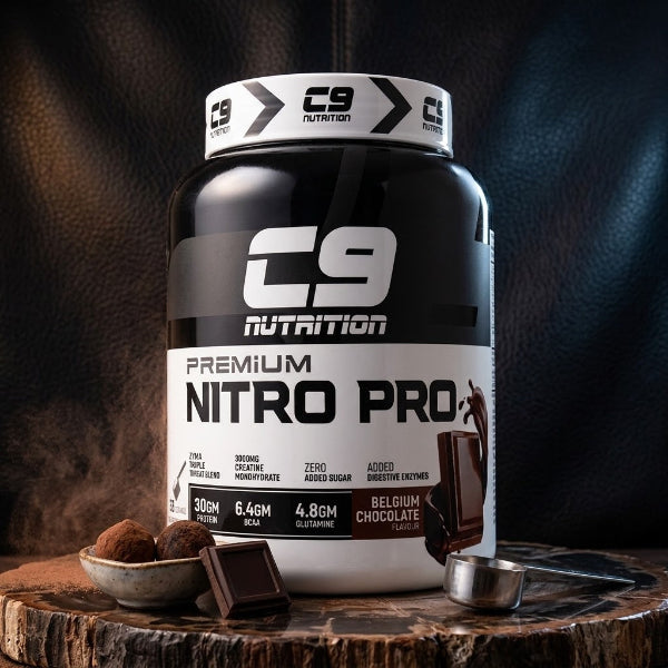 A large tub of C9 Nutrition Premium Nitro Pro powder in Belgium Chocolate flavor, styled on a rustic wooden block with chocolate pieces and cocoa powder against a dark textured background.