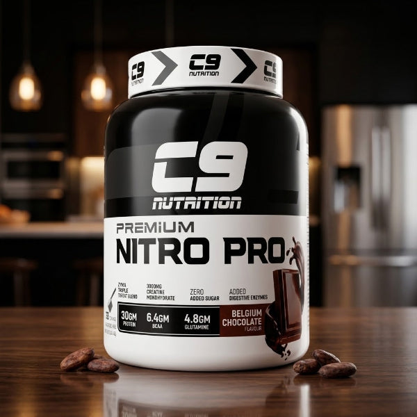 A tub of C9 Nutrition Premium Nitro Pro in Belgium Chocolate flavor sits on a wooden countertop with chocolate pieces scattered around it. The background is a blurred kitchen setting.